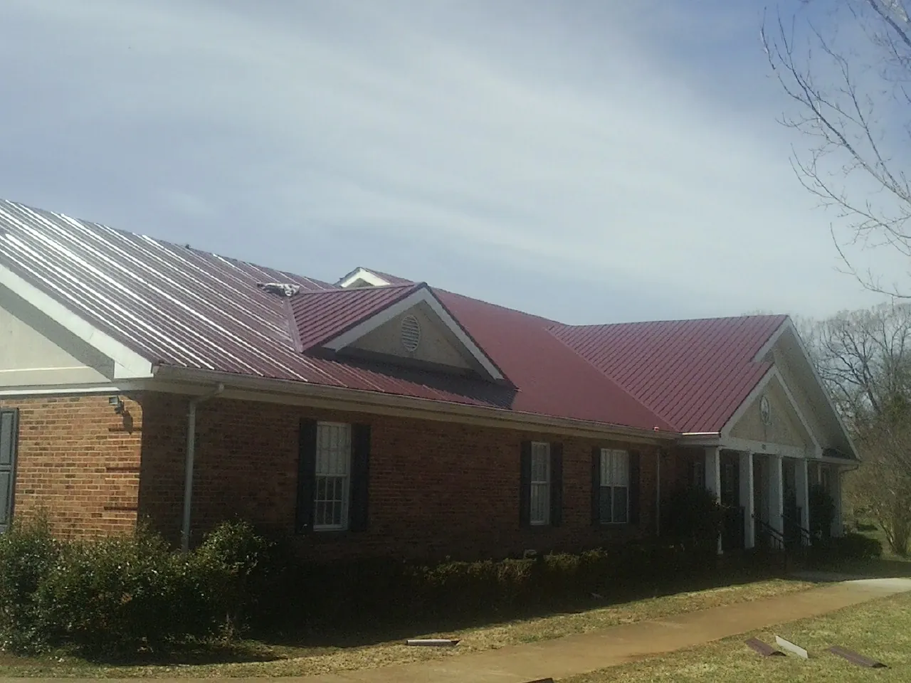Red metal roof with gabled entries on a long brick building, from a Hail Damage Roof Repair job in Palomar Mountain