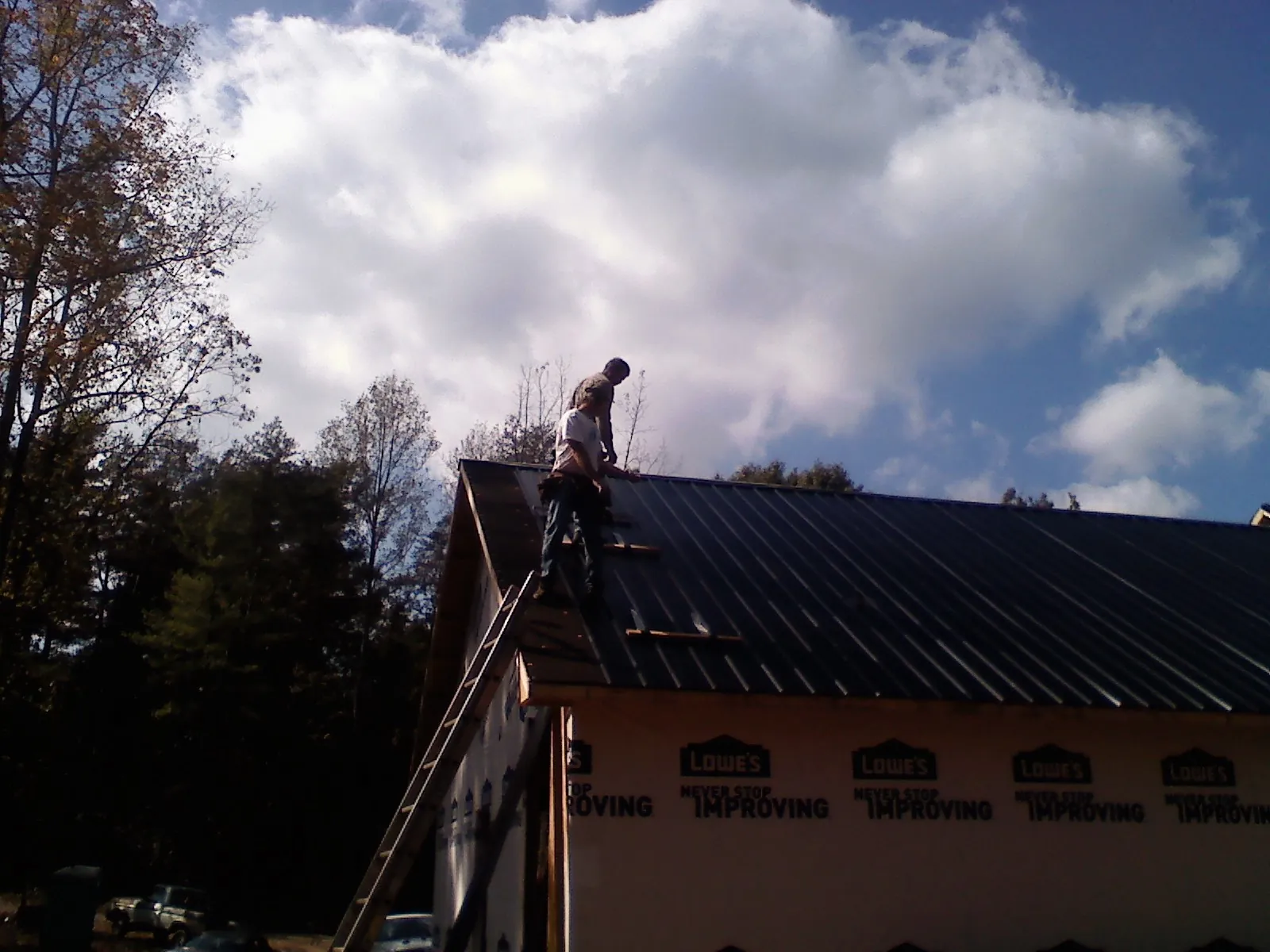 Roofer fastening dark metal panels high against a cloudy sky, from a Roof Inspection job in Palomar Mountain